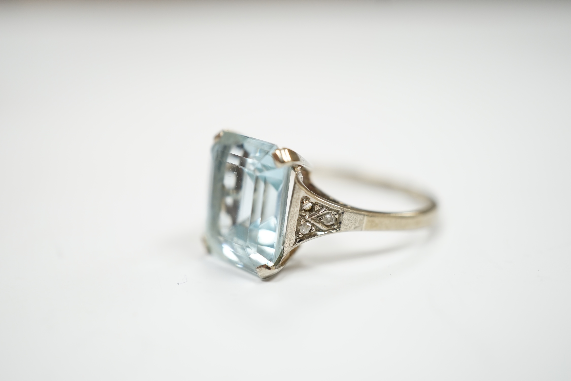 A white metal and single stone emerald cut aquamarine set ring, with rose cut diamond chip set shoulders (one stone missing), size M, gross weight 3.2 grams.